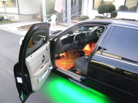 2003 Ford Crown Victoria - Close view through open front door of black sedan, tan door panel and seats with green underglow on pavement