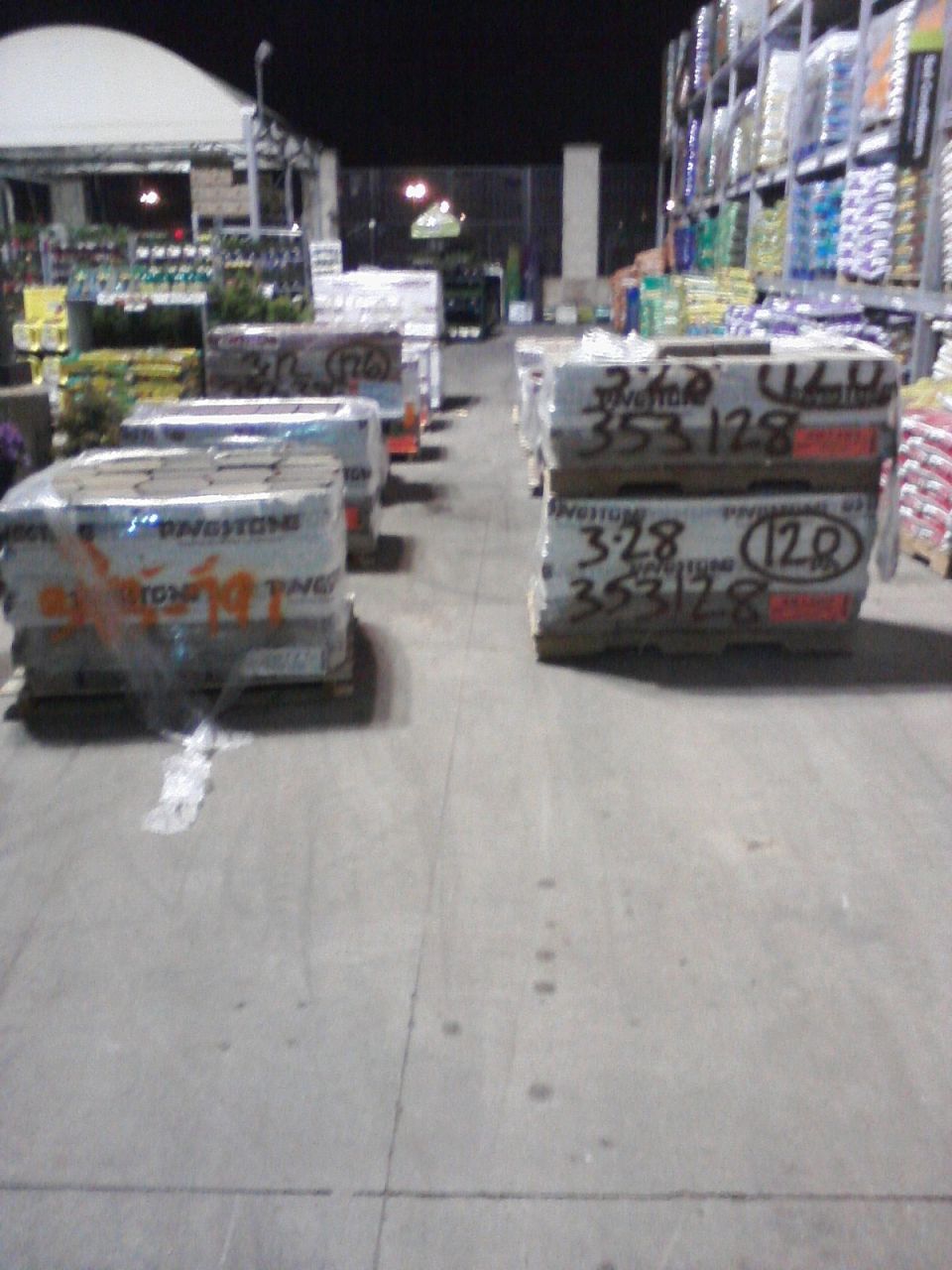 Pallets of paving stones wrapped in plastic sit on wooden pallets in a store aisle at night
