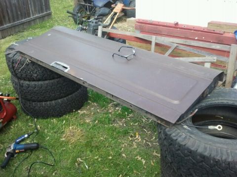 1979 Ford Bronco - A rusty tailgate is displayed outdoors, supported by stacked tires, with safety glasses placed on its surface.
