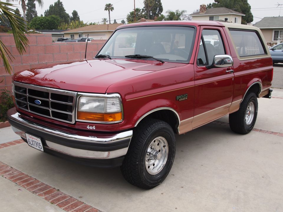 Red Ford Bronco parked in driveway. Has a tan trim and 4x4 badge