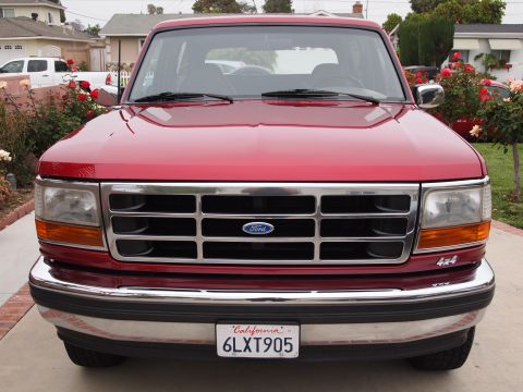 1994 Ford Bronco - Red Ford Bronco with a chrome grille and bumper, seen from the front. The 4x4 badge is visible on the fender.