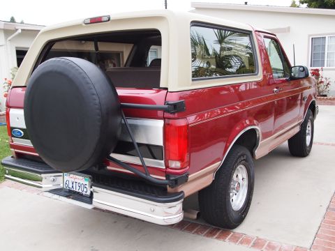 1994 Ford Bronco - This two-tone red and tan 1994 Ford Bronco is shown from the rear, a mounted spare tire and a California license plate.