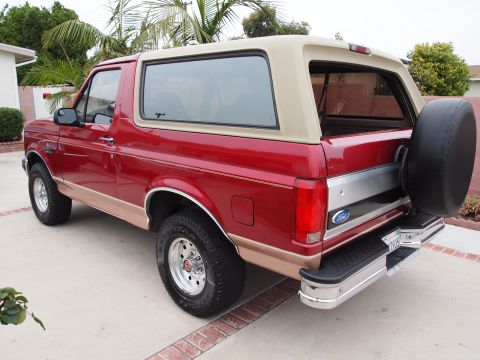 1994 Ford Bronco - Rear view of a red 1994 Ford Bronco with a tan top and a spare tire on the back.