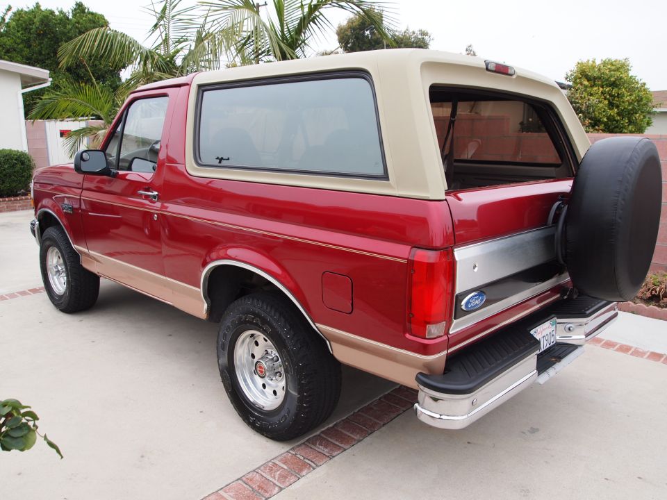 1994 Ford Bronco, red with tan removable top, seen from rear 3/4 angle. Spare tire mounted on rear door