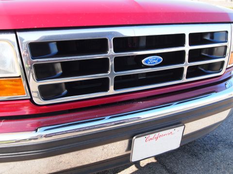 1994 Ford Bronco - Close-up of a red Ford truck's front grille, chrome horizontal bars and the iconic Ford emblem.