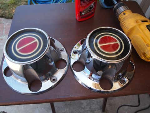 1994 Ford Bronco - Two chrome hubcaps with red and black emblems are displayed on a table next to a drill and a bottle of car cleaner.