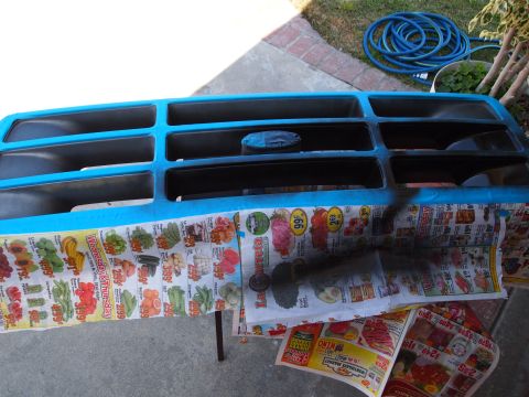 1994 Ford Bronco - A vehicle grille is being spray-painted black, with blue painter's tape protecting areas not to be painted.