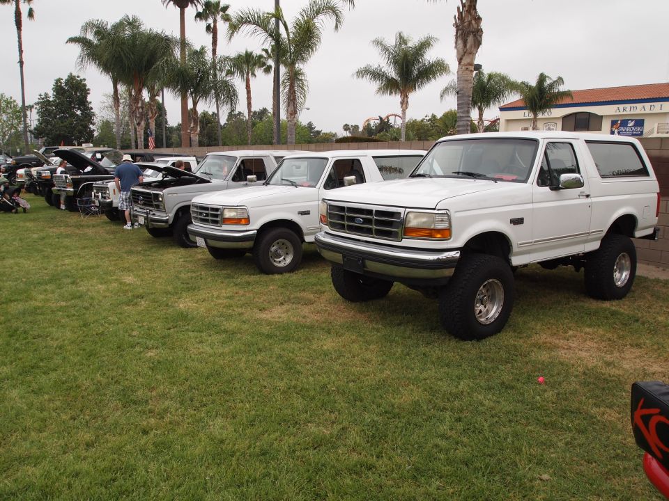 White lifted Ford Bronco, front 3/4 view, parked on grass with other vehicles