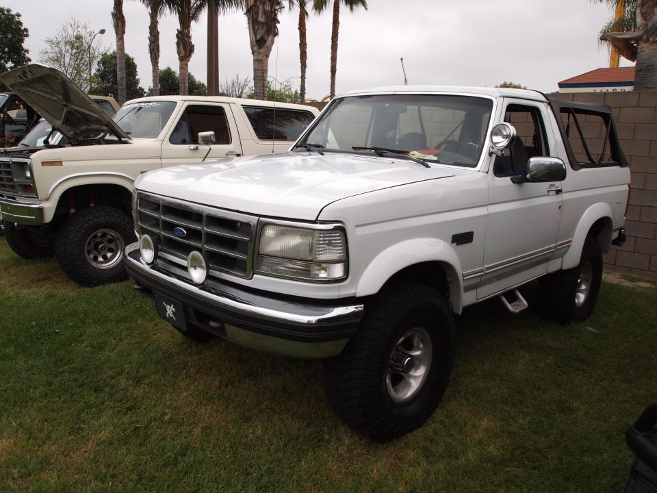 White 1994 Ford Bronco with off-road tires parked next to another Bronco
