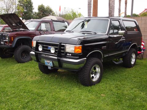 1994 Ford Bronco - A black Ford Bronco is parked on grass next to another SUV with its hood up.