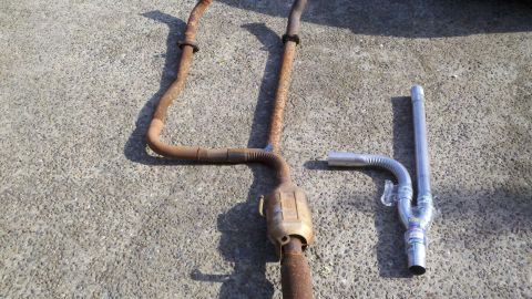1978 Ford Bronco - Rusty and new exhaust system components are displayed on a concrete surface.