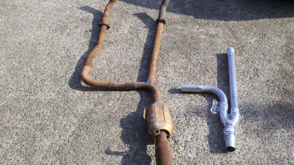 Two exhaust systems, one rusty and one new, laid out on concrete
