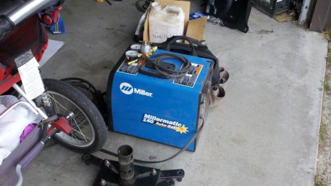 1978 Ford Bronco - A blue Miller welding machine sits on a concrete surface next to a stroller wheel and a plastic jug.
