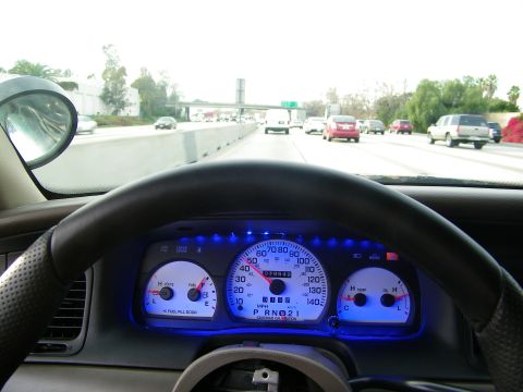 2003 Ford Crown Victoria - Driver POV on highway with side mirror, traffic ahead and blue-illuminated dashboard