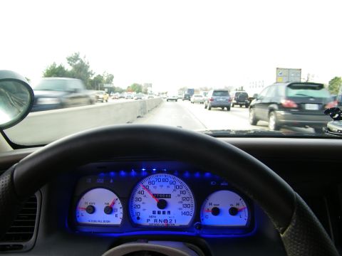 2003 Ford Crown Victoria - Driver view of highway with concrete barrier and cars, blue glowing gauges and side mirror