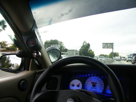 2003 Ford Crown Victoria - Driver view showing A-pillar gauge, tan trim, steering wheel and highway traffic ahead