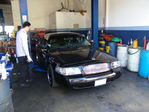 2003 Ford Crown Victoria - Front of black sedan with chrome billet grille on a shop lift, technician standing beside it