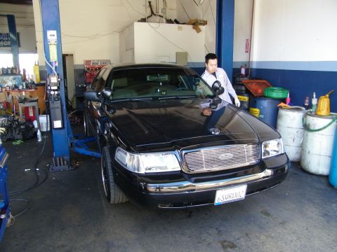 2003 Ford Crown Victoria - Technician detailing the hood of a black full-size sedan on a lift, billet grille and front plate visible