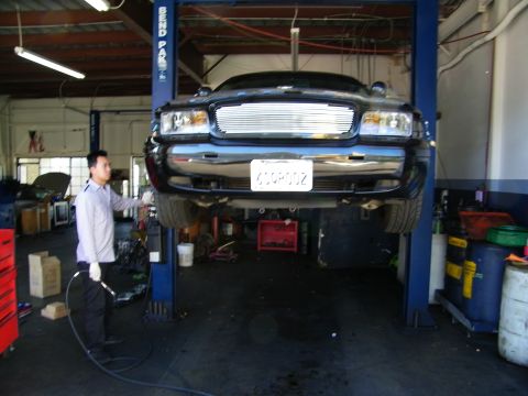 2003 Ford Crown Victoria - Black truck-based SUV on a shop lift, technician working at the front bumper