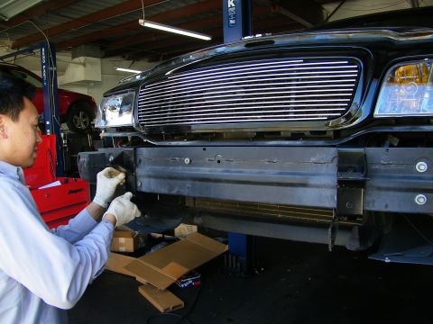 2003 Ford Crown Victoria - Gloved technician fitting hardware to the front of a black billet-grille truck