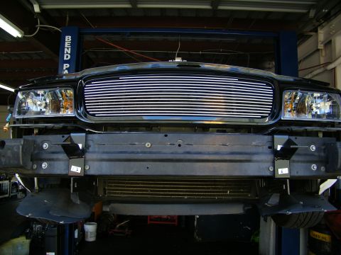2003 Ford Crown Victoria - Black truck front showing chrome billet grille and bare bumper mounting points on a lift