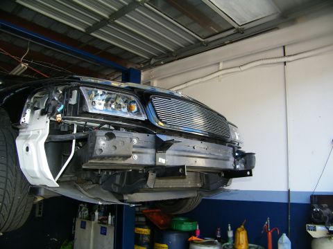 2003 Ford Crown Victoria - Black truck raised with billet grille and front clip partly disassembled in a shop