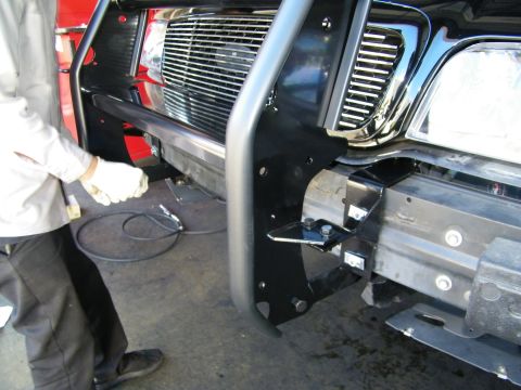 2003 Ford Crown Victoria - Gloved worker handling wiring beside a newly mounted black grille guard on a truck