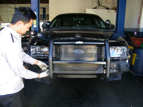 2003 Ford Crown Victoria - Worker fitting a chrome grille guard to a Ford truck front with billet grille and blue oval