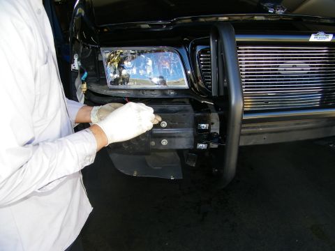 2003 Ford Crown Victoria - Gloved technician at the headlight while a black grille guard sits on the Ford truck front