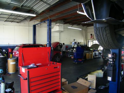 2003 Ford Crown Victoria - Service bay showing a red rolling tool cabinet, lifted vehicle and tire at right under shop lighting