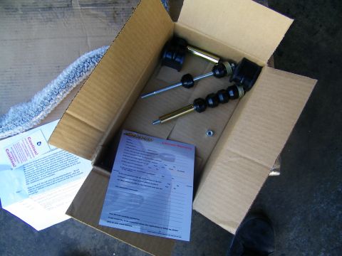 2003 Ford Crown Victoria - Pair of shock or strut units in a carton beside a printed warranty form on concrete