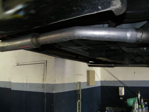 2003 Ford Crown Victoria - Underbody view of a bright mandrel-bent exhaust pipe running beneath the floorpan against shop wall