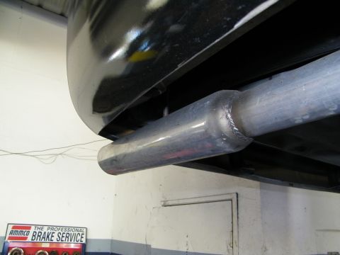 2003 Ford Crown Victoria - Fresh exhaust pipe weld under a vehicle, with an AMMCO Professional Brake Service sign on the wall