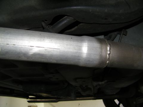 2003 Ford Crown Victoria - Detail of a fabricated exhaust pipe weld seam routed under the floorpan of a lifted vehicle