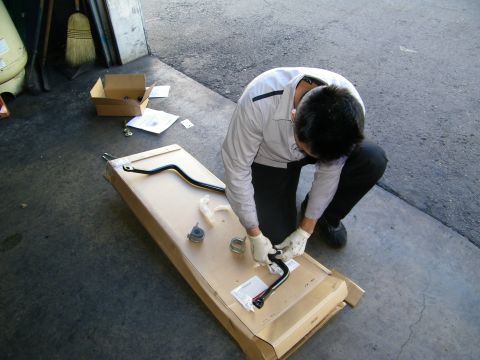 2003 Ford Crown Victoria - Worker with gloves unpacking a curved black anti-roll bar and bushings from a long carton