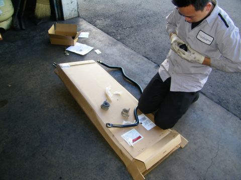 2003 Ford Crown Victoria - Gloved technician examining a black anti-roll bar with mounting bushings laid out on cardboard