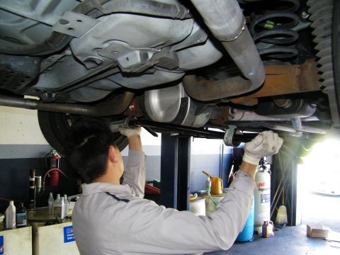 2003 Ford Crown Victoria - Worker installing parts under a lifted vehicle, hands at the floorpan with suspension and exhaust overhead