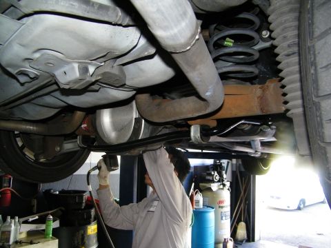 2003 Ford Crown Victoria - Worker reaching into the undercarriage near the exhaust with coil spring, axle and fuel tank overhead