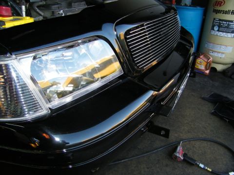 2003 Ford Crown Victoria - Driver-side front clip of black car showing billet grille and headlight, air hose on floor