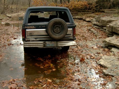 1982 Ford Bronco - A Ford Bronco is parked in a shallow stream bed covered with fallen leaves.