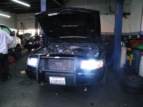 2003 Ford Crown Victoria - Front of black car with grille guard and billet grille, headlights lit, tech working at left