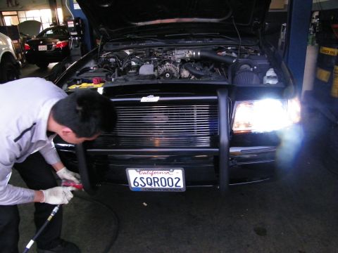 2003 Ford Crown Victoria - Worker in gloves uses pneumatic tool at push-bar bumper of black car with hood up