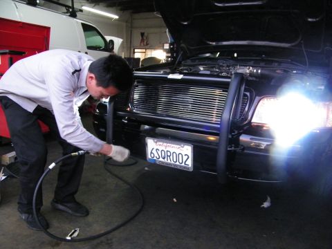 2003 Ford Crown Victoria - Technician leaning into push-bar guard area of black car with air line in dim shop