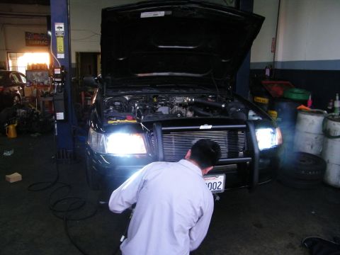 2003 Ford Crown Victoria - Front of black car with grille guard and twin headlights in busy repair shop bay
