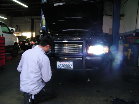 2003 Ford Crown Victoria - Worker in white shirt crouched at billet grille of black car with hood open on lift