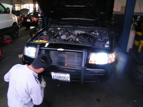 2003 Ford Crown Victoria - Technician at push-bar guard of black car with headlights lit and engine exposed