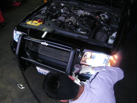 2003 Ford Crown Victoria - Technician leaning into front of black car, headlight and intake visible under open hood