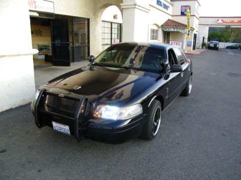 2003 Ford Crown Victoria - Blacked-out sedan with push-bar grille guard parked outside shops with V-TEC signage