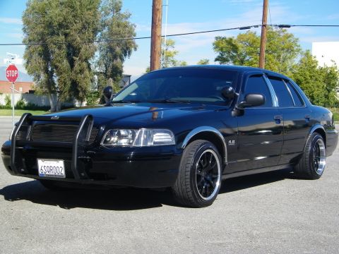 2003 Ford Crown Victoria - Blacked-out sedan on black rims and grille guard parked near stop sign and trees