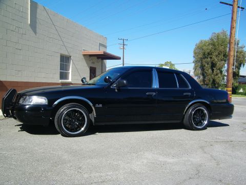 2003 Ford Crown Victoria - Side view of blacked-out four-door sedan on dark rims beside concrete building